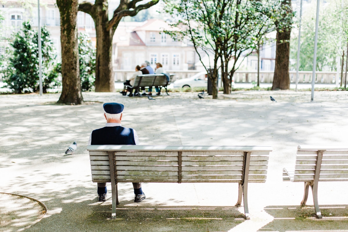 An elderly man sitting on a bench in a Guimarães park, with the town historic buildings behind him